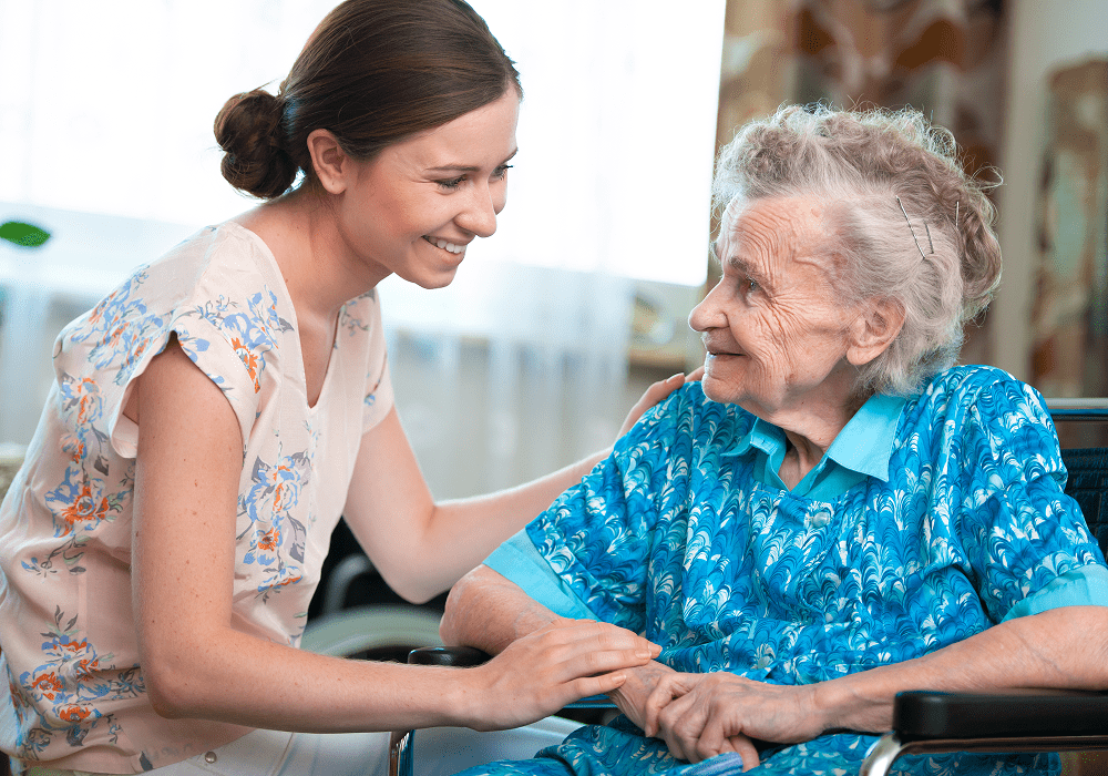 Caregiver smiling at elderly woman in blue.